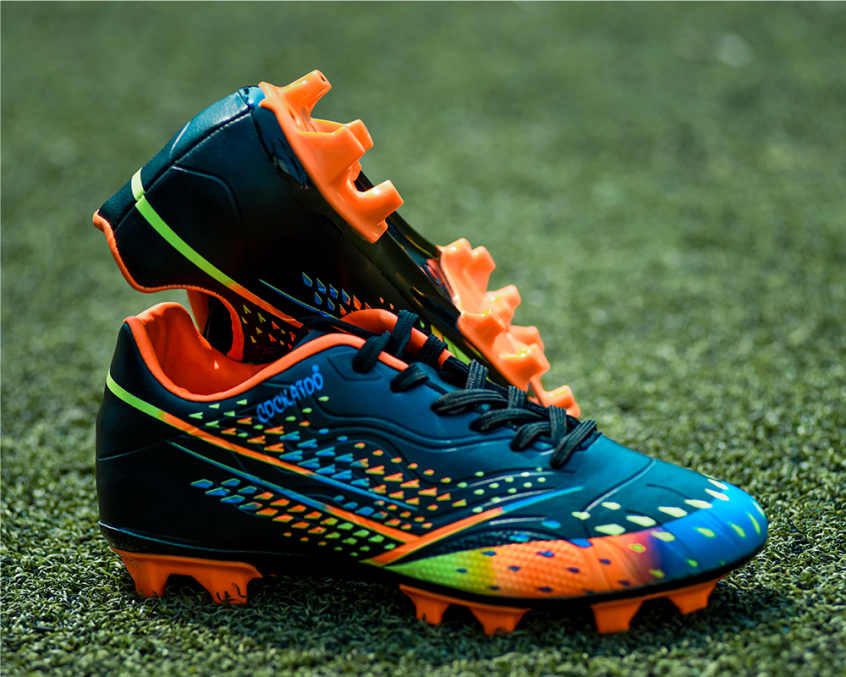 A pair of football shoes with a synthetic leather upper in black, blue, orange, and green colors, featuring a die-cut soft cushion sockliner and a high shear strength TPU sole for stability and traction.