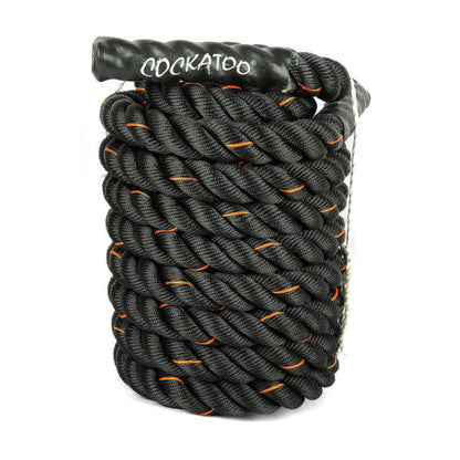 A coiled black and orange battle rope with the brand name 'COCKATOO' visible on the black rope, packed in a brown box.